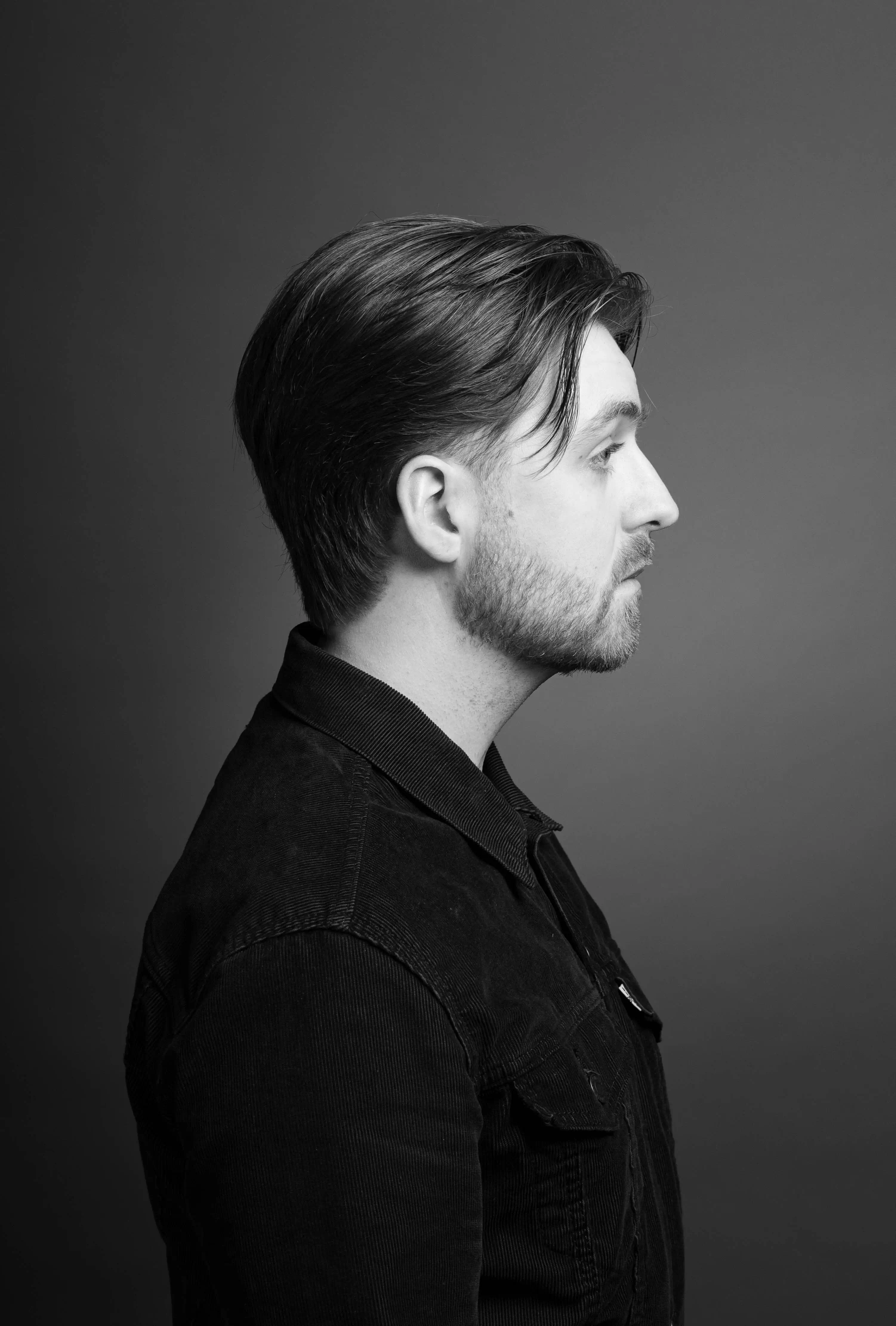 Man with curtain style haircut with beard and denim jacket looking to the right